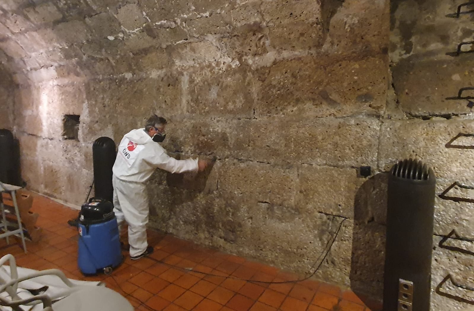ÖWD Mitarbeiter entfernt weißen Schimmel von einer alten, feuchten Natursteinmauer mit Spezialausrüstung