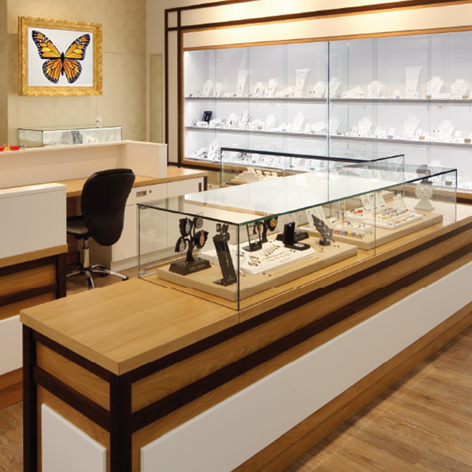 Eine moderne Schmuckvitrine in einem Geschäft mit ausgestellten Armbanduhren und Schmuckstücken sowie einem Schmetterlingsbild an der Wand.