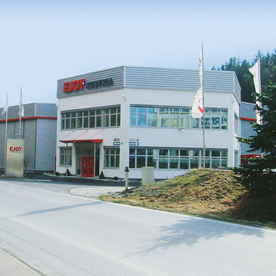Industriegebäude mit EJOT Austria-Logo und Flaggen davor.