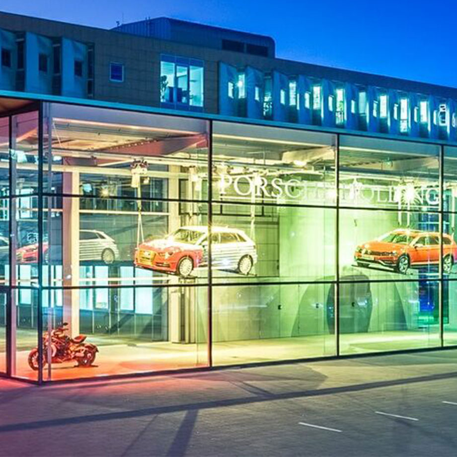 Außenansicht des Schaufensters der Porsche Holding in Salzburg mit beleuchteten Autos im Inneren und einem Motorrad im Vordergrund.